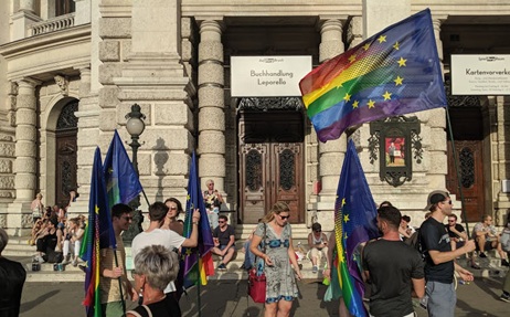 People holding up pride flags in the street outside a building.