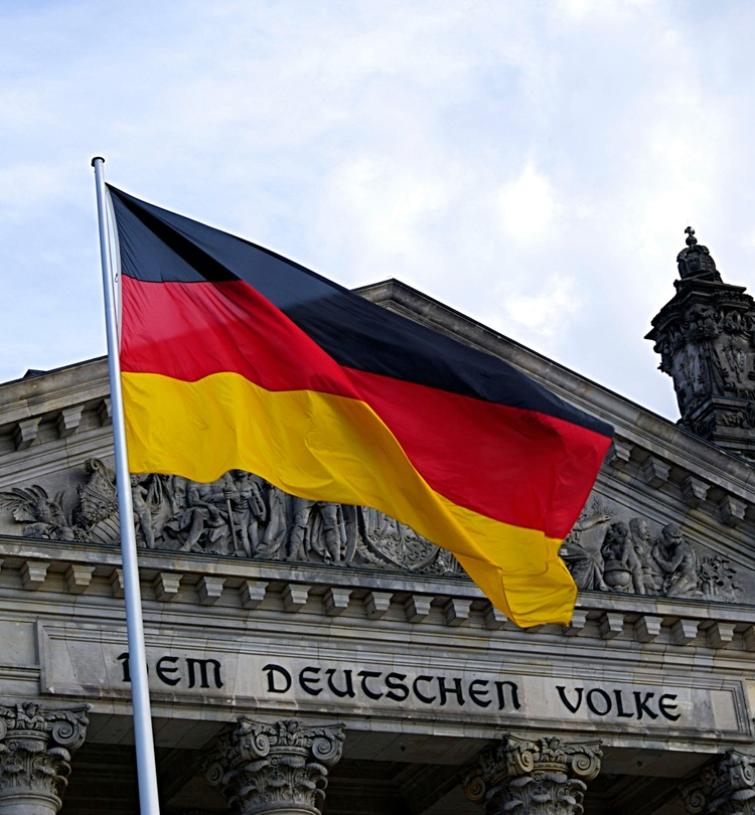 German flag waving in front of a building with German inscripted in the stone.